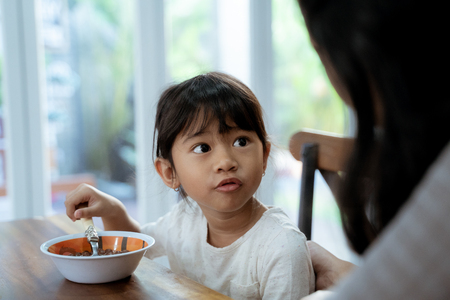 Little asian girl eating cereal for breakfast with momの写真素材