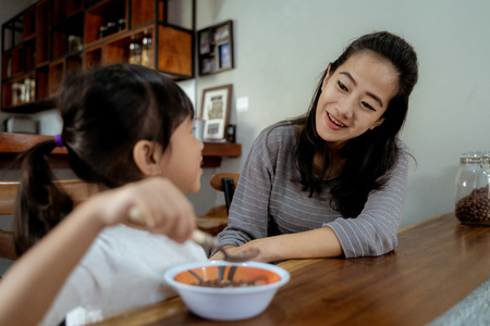 Little asian girl eating cereal for breakfast with momの写真素材