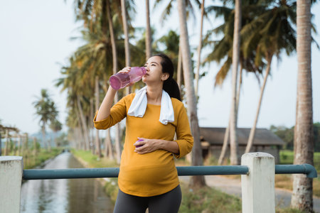 pregnant woman after workout drinking a bottle of waterの写真素材