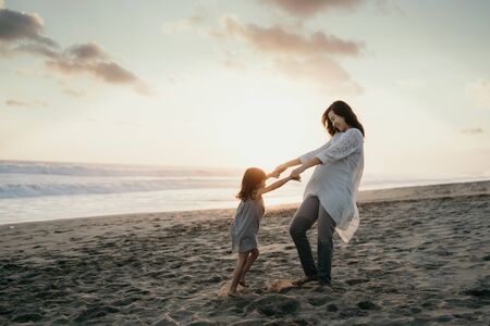 young beautiful pregnant woman with her little cute daughter playing in the beachの写真素材