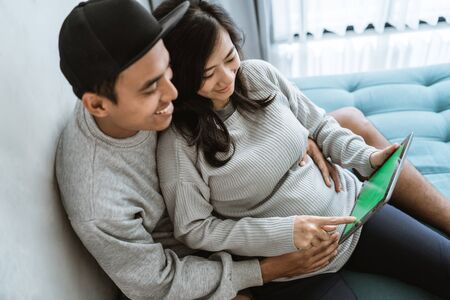 happiness of couples holding the wifes pregnant stomach while using digital tabletの写真素材