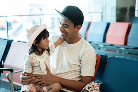 little girl on his fathers lap while waiting for a flight