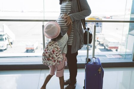 Asian pregnant women and their daughter stand holding stomachの写真素材