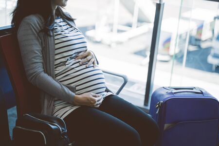 pregnant women sit holding their stomach in the airport waiting roomの写真素材