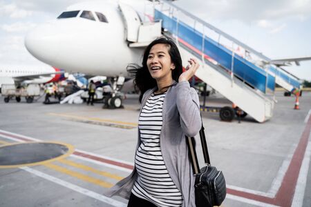 asian pregnant woman standing pulling suitcaseの写真素材