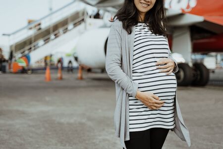 Asian pregnant women standing beside a suitcases on the runwayの写真素材