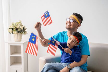 father and son holding malaysian flag together while watching soccer matchの写真素材