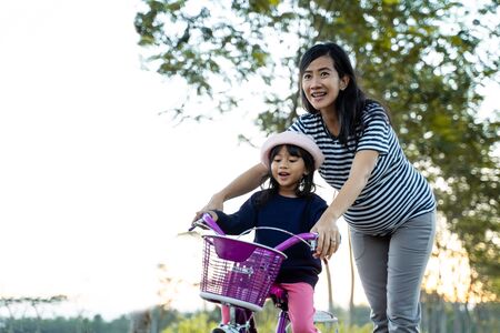 Kid learning to ride bicycle with motherの写真素材