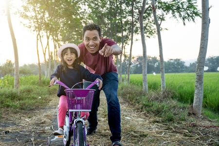 Daughter learning to ride bicycle with daddyの写真素材