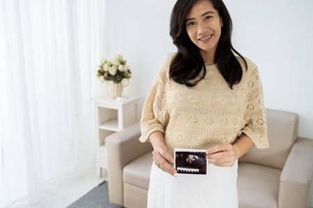 Asian pregnant young woman holding ultrasound scanの写真素材