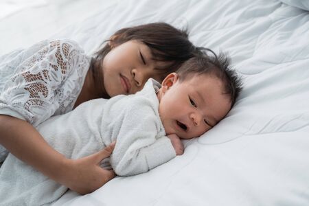 smiling happy girl sibling infant lying on bedの写真素材