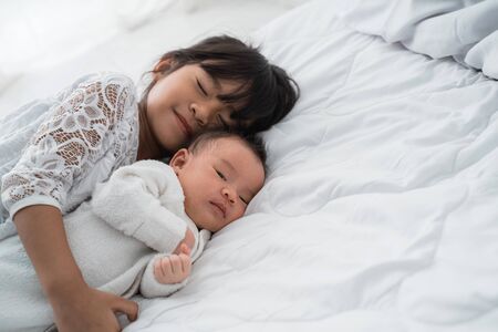 daughter kid with infant sibling playing on bed wearing whiteの写真素材