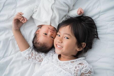 smiling happy girl sibling infant lying on bedの写真素材