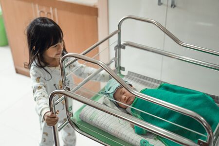 Newborn baby laying in crib accompanied by his sisterの写真素材