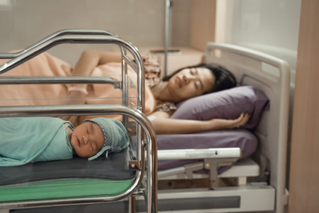 Newborn baby laying in crib with his mother lying on bed side