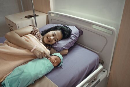Asian newborn baby laying in crib with his motherの写真素材