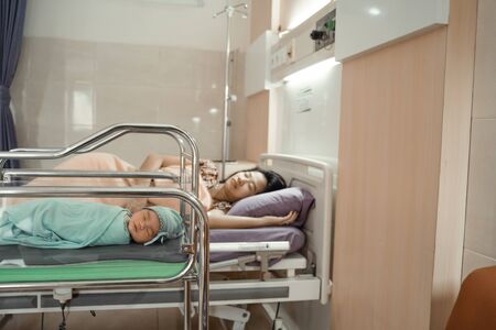 Asian newborn baby laying in crib with his mother lying on bed sideの写真素材