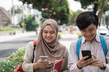 two college student walking together and holding smartphoneの写真素材