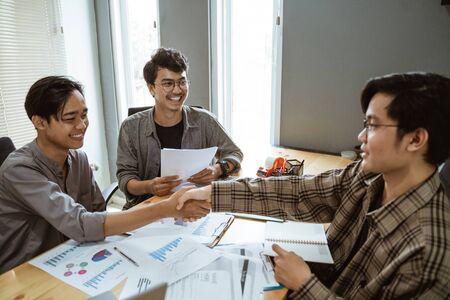asian business partner shaking hand during meeting in creative spaceの写真素材