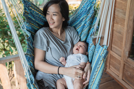 mother holding daughter while resting on hammock