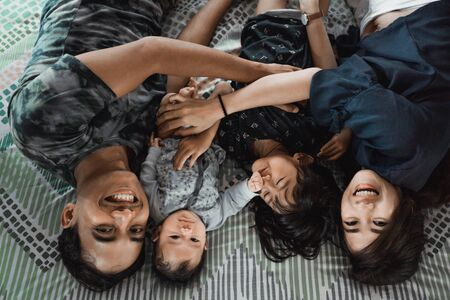 Asian young family lying with embrace on the bedの写真素材