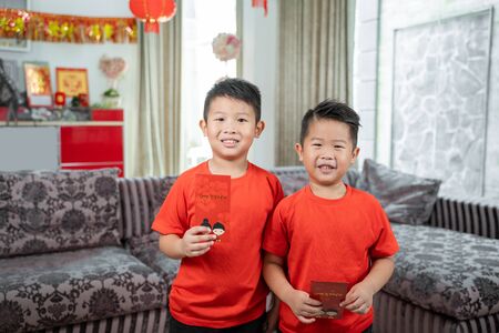 two asian chinese boys smile wearing red shirts with angpauの写真素材