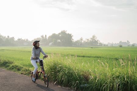Asian women wear helmets to ride folding bikes in the rice fields in the morningの写真素材