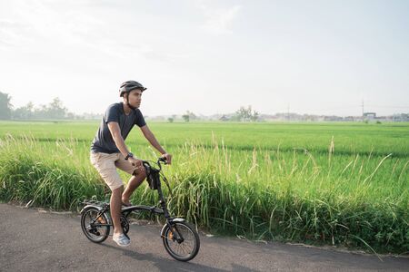 Asian young male wear helmets to ride folding bikes in the rice fieldsの写真素材