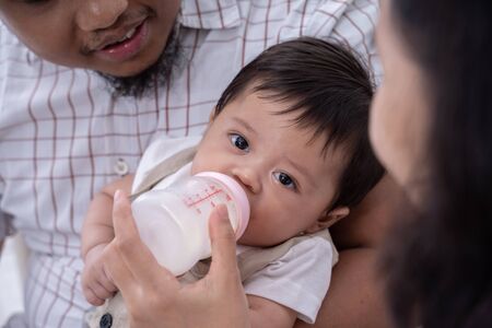 asian mother feeding son with milk in baby bottleの写真素材