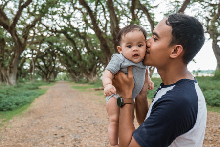 asian father kissing while holding up a baby
