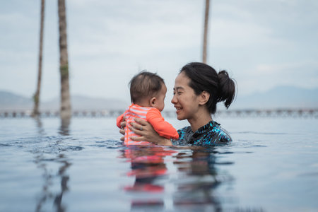 mother holding her child while swimming in the pool