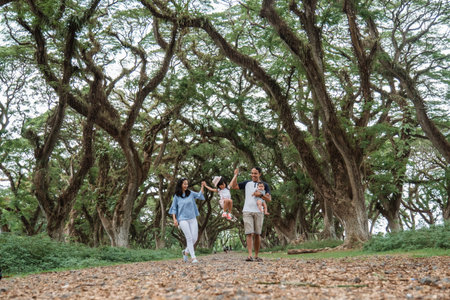 mother and father and two children smile walking through the big trees, enjoying a vacation in the...