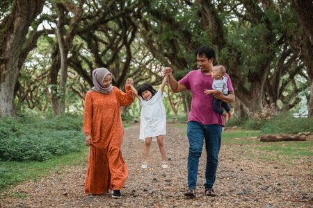 father and mother raise their daughters hands and carry the child while walkingの写真素材