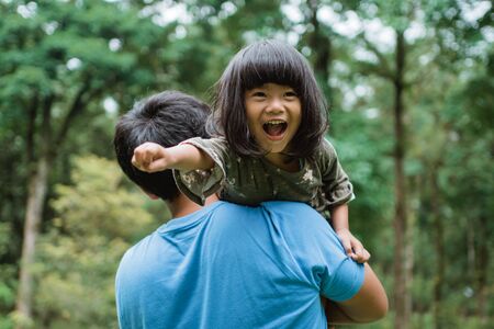 little girl laughed happily when carried on her fathers shoulderの写真素材