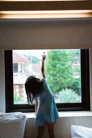 alone little girl reaching window curtainの写真素材