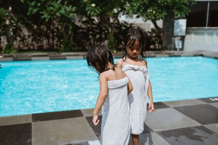 two little girls stand wearing towels beside poolの写真素材