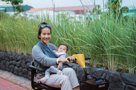 mother smiles holding her baby while driving a buggy carの写真素材