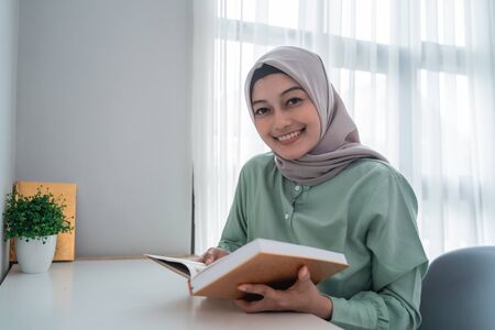 Beautiful young woman wearing a hijab smiling holding the holy book of the Koranの写真素材