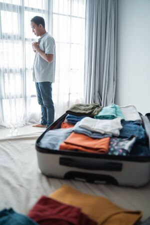 Young Asian man wears a shirt after opening his suitcase in the bedroomの写真素材