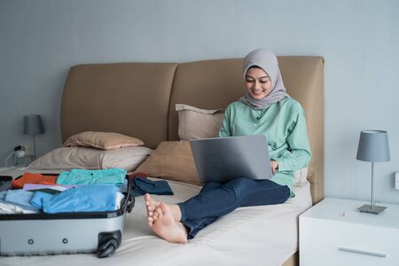 Asian muslim woman using laptop to looking departure schedules via online applicationの写真素材