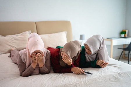 Asian hijab woman with friends cover face because of fear when watching horor filmの写真素材