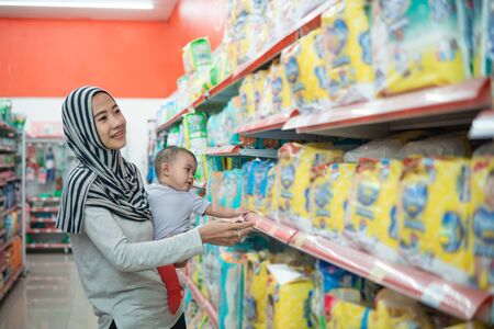 muslim asian mother buying baby product while carrying her daughterの写真素材