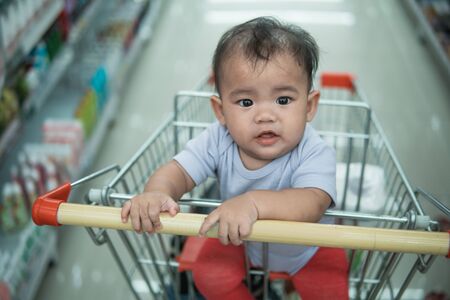 happy infant baby sitting alone in shopping cart or trolley in grocery supermarketの写真素材