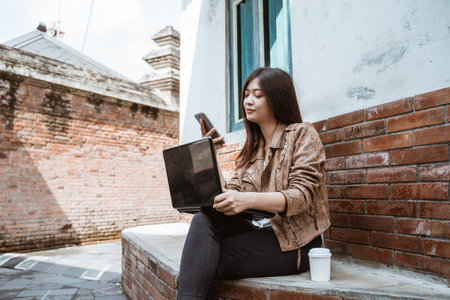 busy woman working with laptop and her mobile phone outdoorの写真素材