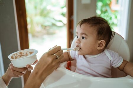 happy asian baby feeding time sitting on highchairの写真素材