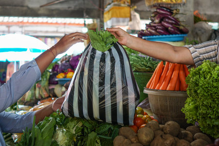 buy vegetables at the vegetable market, cropped images of seller hand provide plastic bags...