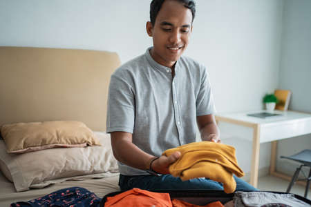 asian man putting his clothes in the suitcaseの写真素材