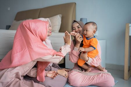Three muslim women enjoy playing with little boy when sitting on the floorの写真素材