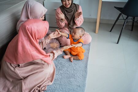 asian muslim mother with her friends enjoy playing with her son when sitting on the floorの写真素材