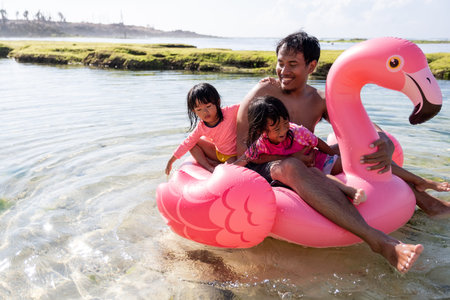 Asian father and two daughters ride flamingo buoy on the beach